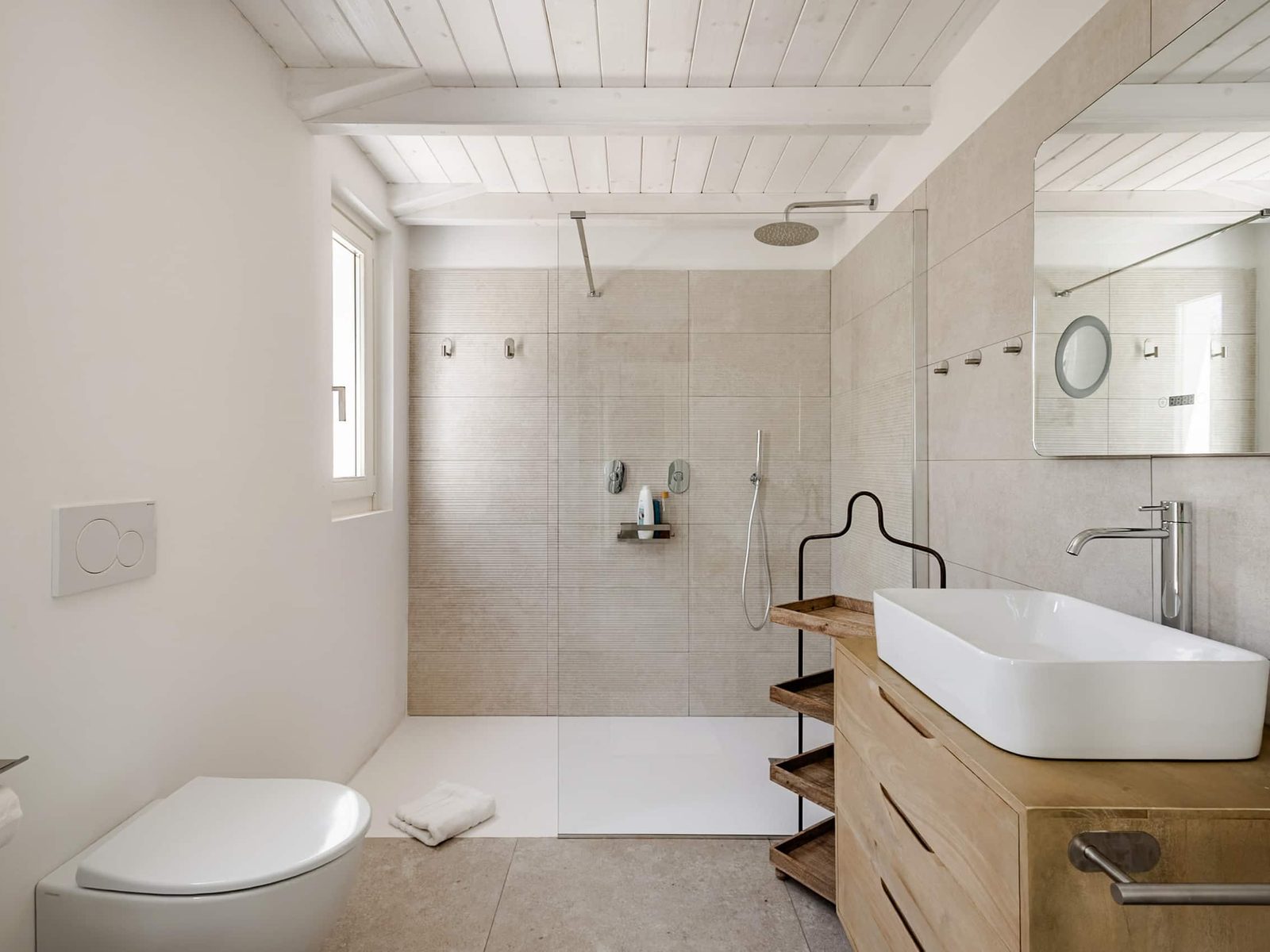 Bagno privato con doccia a filo pavimento, lavabo d'appoggio su mobile in legno e specchio
