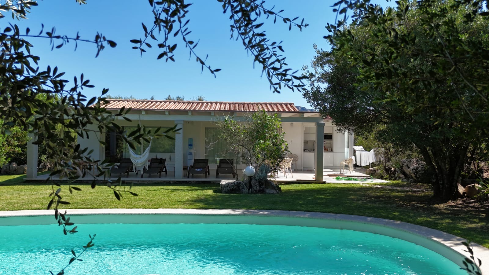 La villa vista dalla piscina, con il portico, l’amaca e i lettini